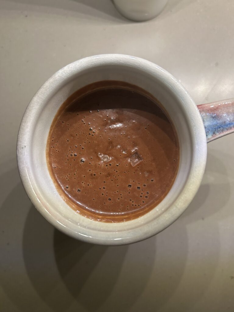 A mug of rich hot chocolate made with dates topped with a pinch of flaky sea salt.