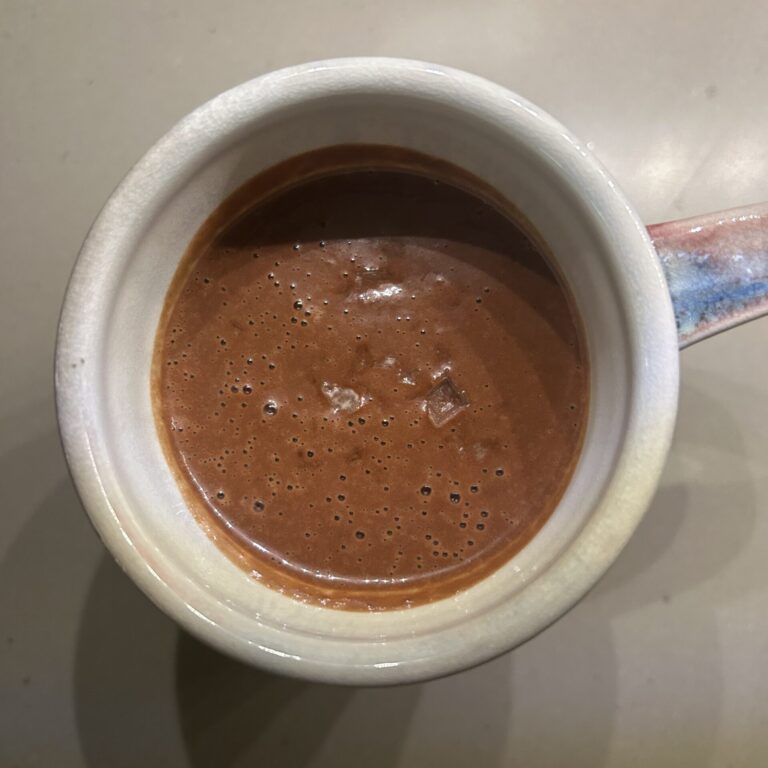 A mug of rich hot chocolate topped with a sprinkle of flaky sea salt.