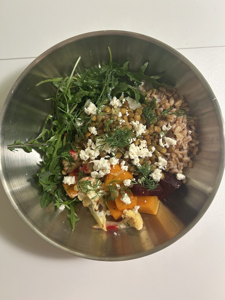 A grain bowl with roasted root vegetables, farro, lentils, arugula, and a garnish of goat cheese and dill.